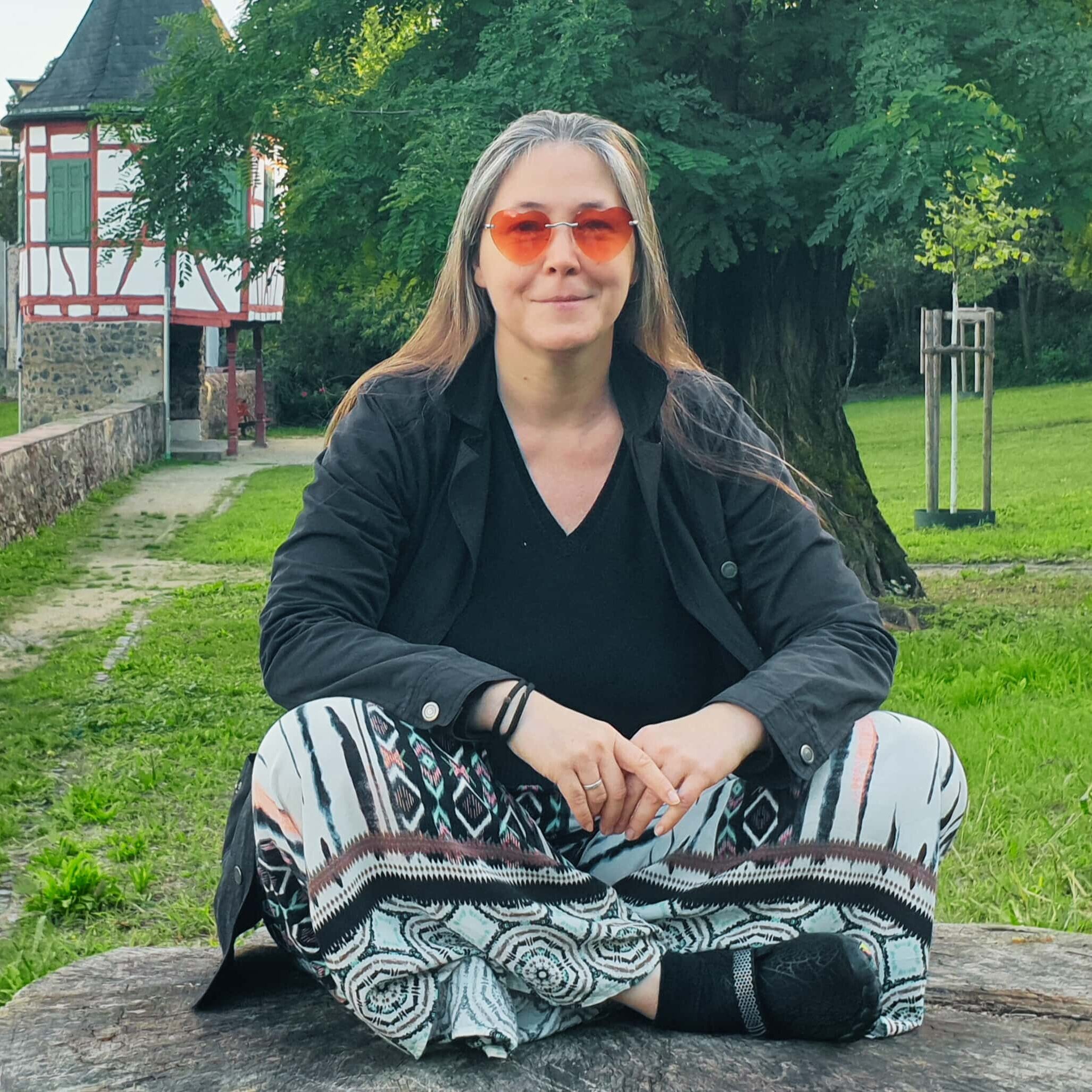 Elke Raab sitzt auf einem rieseigen Baumstumpf im Steinheimer Kräutergarten